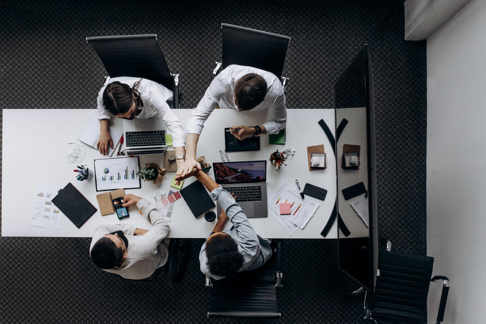 Four colleagues high-fiving over a desk of laptops and charts